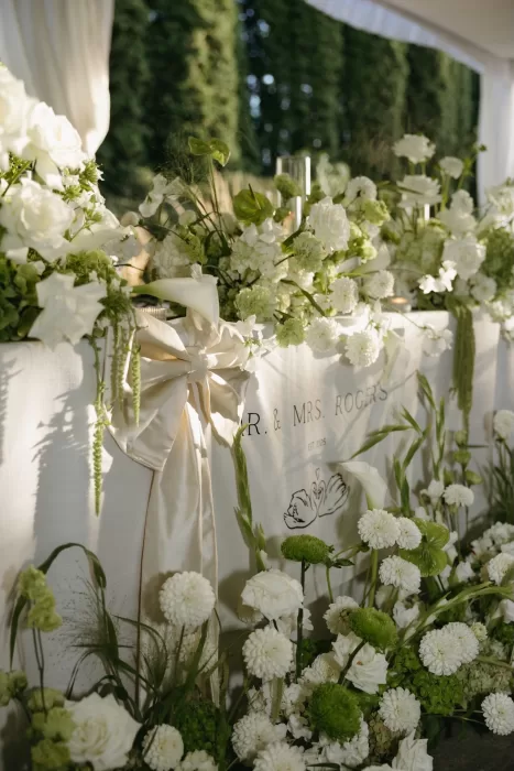 Lush white and green floral arrangements decorate the head table at Chateau Lill, creating a fresh and romantic reception setting.