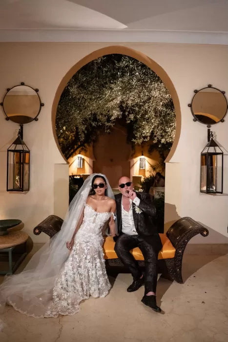 Bride and groom wearing sunglasses seated beneath an arched doorway at Jnane Tamsna during their evening celebration.