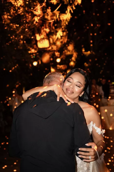 Bride embracing a guest under warm golden lights, with sparkling reflections creating a magical nighttime atmosphere at Jnane Tamsna.