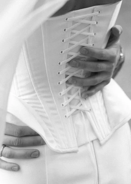 Close-up of a bride fastening her corset dress during wedding preparations at Malpils Manor, captured in soft natural light.