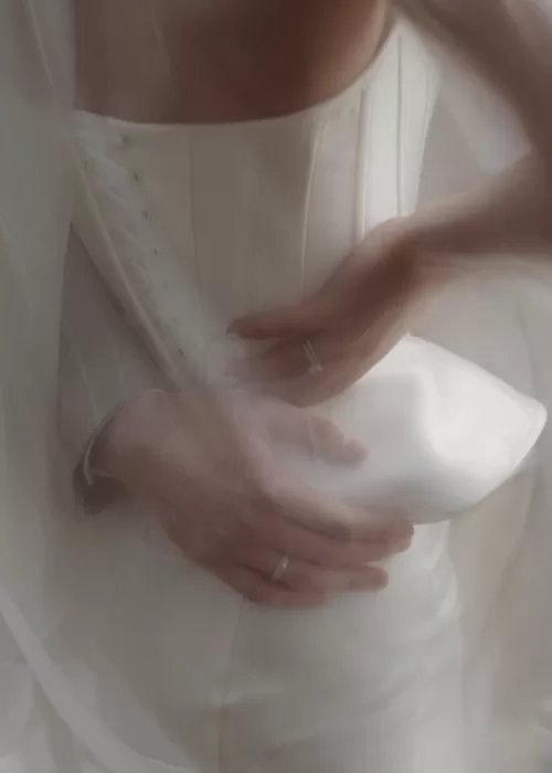 Close-up of a bride fastening her corset dress during wedding preparations at Malpils Manor, captured in soft natural light.
