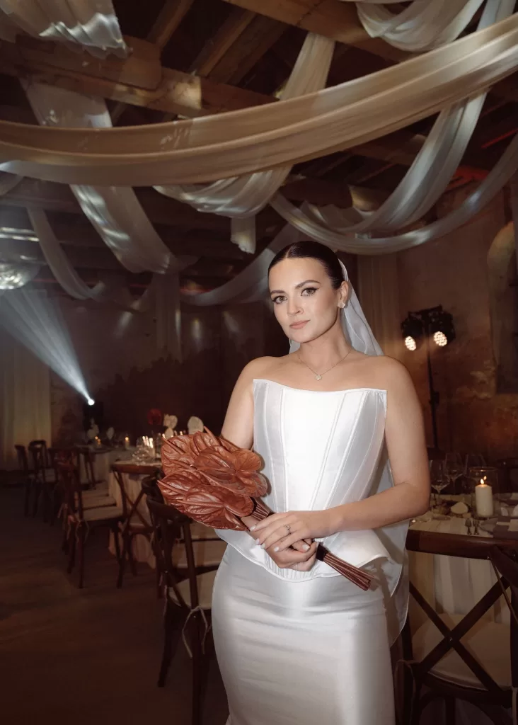 Bridal portrait inside Malpils Manor, with the bride holding a modern bouquet beneath draped fabric and atmospheric lights.