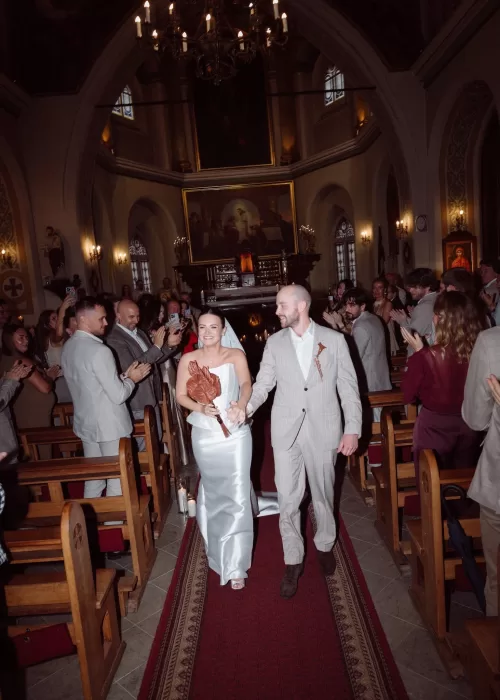 Bride and groom walking back down the church aisle after their Malpils Manor wedding ceremony, greeted by applauding guests.