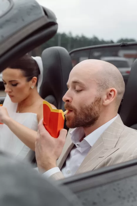 Bride and groom enjoying fries while sitting in a convertible car after their Malpils Manor wedding, captured in a candid moment.