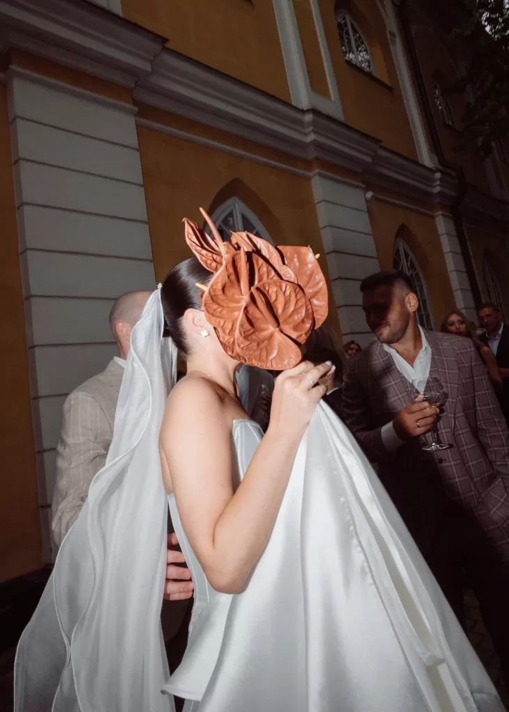 Bride holding her bouquet during an evening wedding celebration outside Malpils Manor, surrounded by guests and warm light.