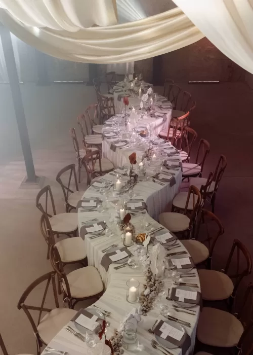 Long banquet table set for a wedding reception at Malpils Manor, styled with candles, soft linens and sculptural florals under flowing drapery.