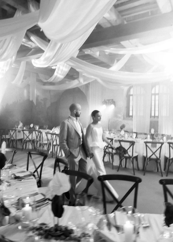 Bride and groom walking through the Malpils Manor reception space, captured candidly among candlelit tables and soft draping.