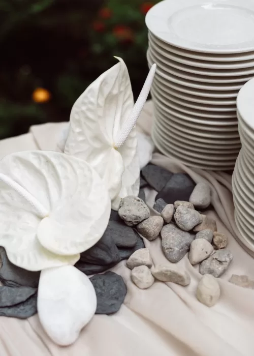 Wedding table detail at Malpils Manor with stacked plates, white anthurium florals and natural stone styling.
