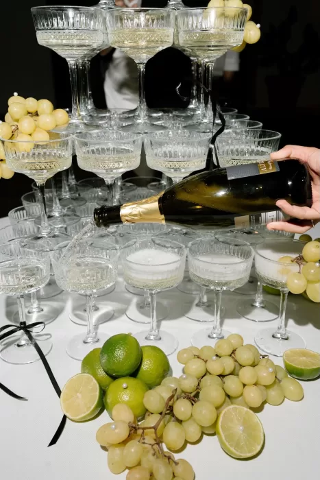 Close-up of champagne being poured into coupe glasses surrounded by limes and grapes at a Masseria celebration.