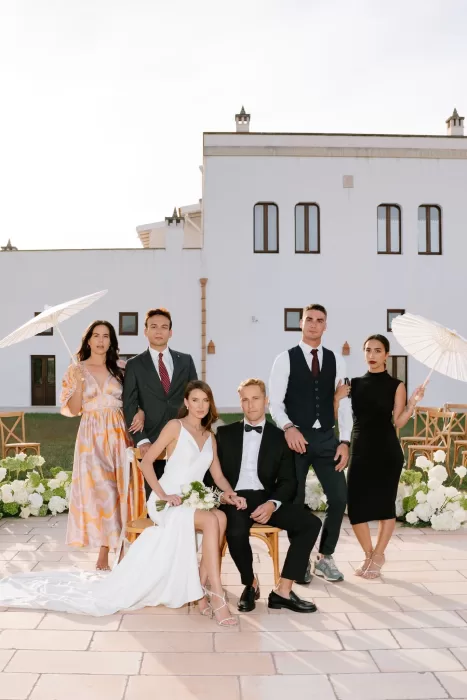 Bridal party posing elegantly outdoors at Masseria with the bride and groom seated among white florals.
