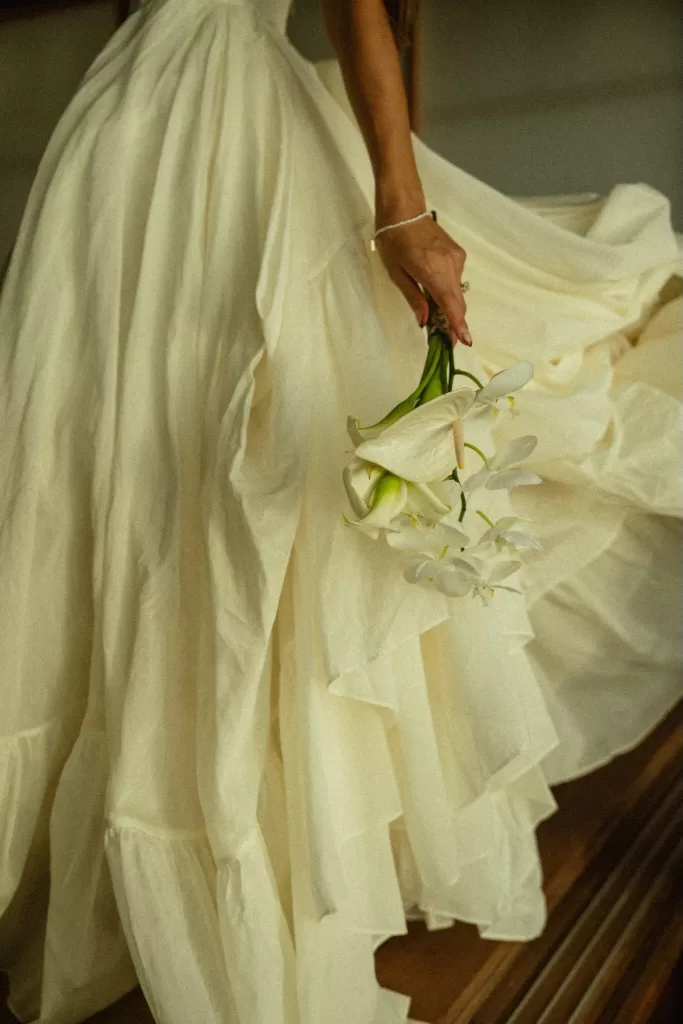 Bride holding a minimalist white bouquet beside her dress, showcasing refined wedding details at Ossipoff’s Cabin.