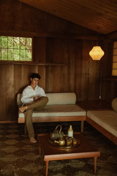 Groom seated inside the warm wooden interior of Ossipoff’s Cabin, surrounded by minimal furnishings and natural textures.
