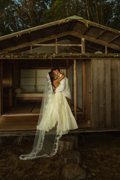 Bride and groom embracing on the wooden porch of Ossipoff’s Cabin, surrounded by forest and warm evening light.