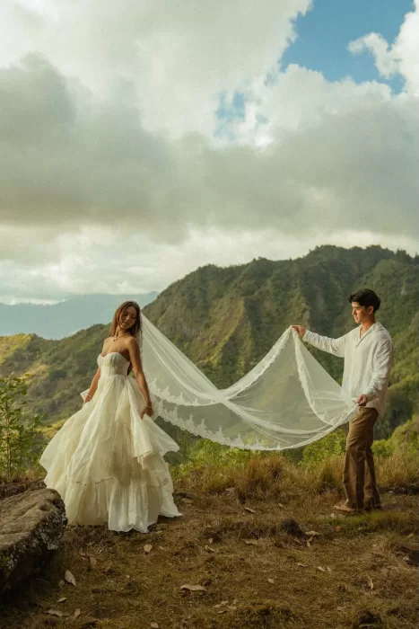 Groom holding the bride’s long veil across a mountain clearing near Ossipoff’s Cabin, highlighting scale and scenery.