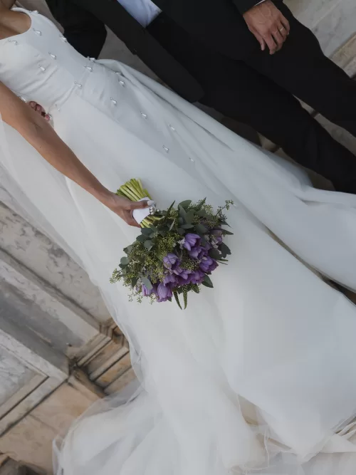 Bride holding a lush purple wedding bouquet against a flowing ivory gown at Vandelli Botanical Garden.
