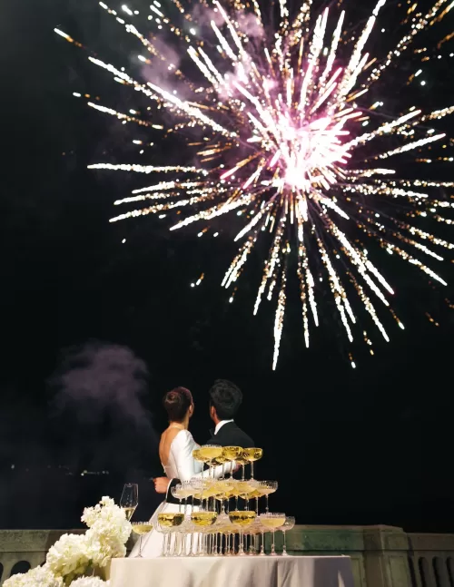 Bride and groom watching fireworks beside a champagne tower overlooking the lake at Villa Lario Resort