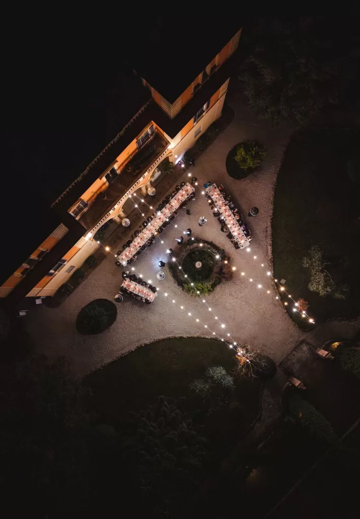 Nighttime aerial view of Villa Lena’s courtyard reception, lit by strings of warm lights above long banquet tables.