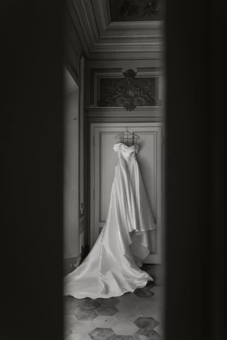 A wedding dress with a long satin train hangs elegantly in an ornate room at Villa Lena.
