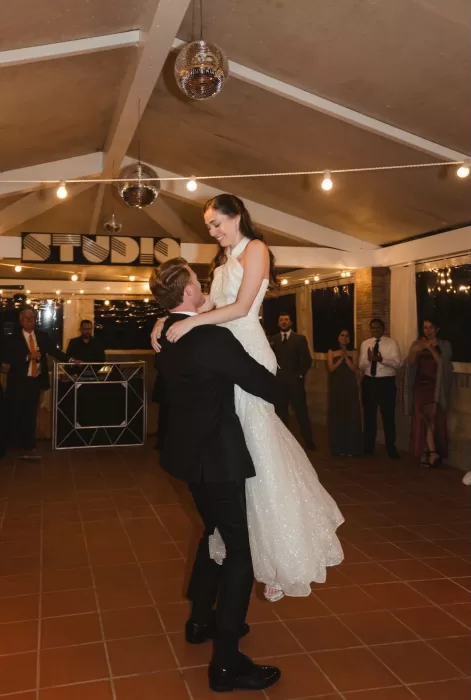 The groom lifts the bride during their joyful first dance under disco balls at Villa Lena.