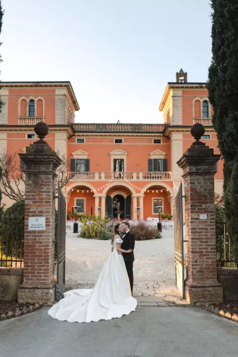 The couple shares a kiss at the entrance gate of Villa Lena, framed by the villa’s terracotta façade.
