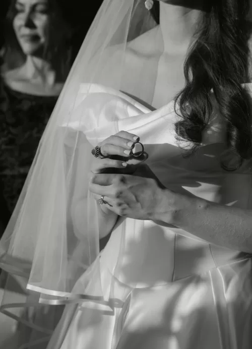 The bride gently holds the wedding rings in soft sunlight, her veil and gown creating elegant shadows at Villa Lena.