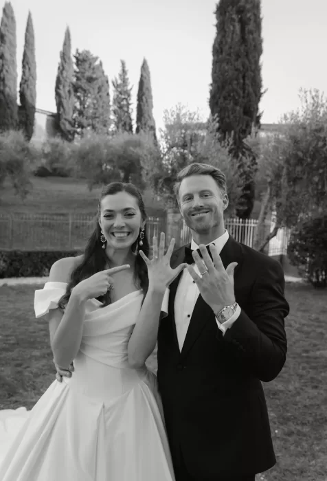 The newlyweds proudly show their wedding rings in a joyful portrait among the cypress trees at Villa Lena.