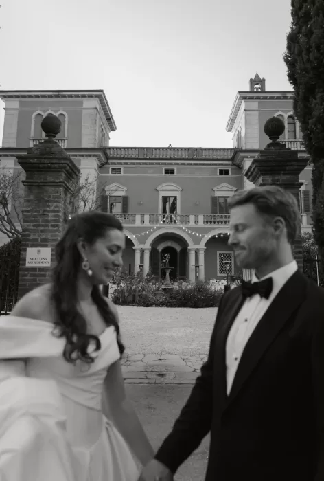 A blurred moment of the couple holding hands in front of the grand Villa Lena façade at sunset.