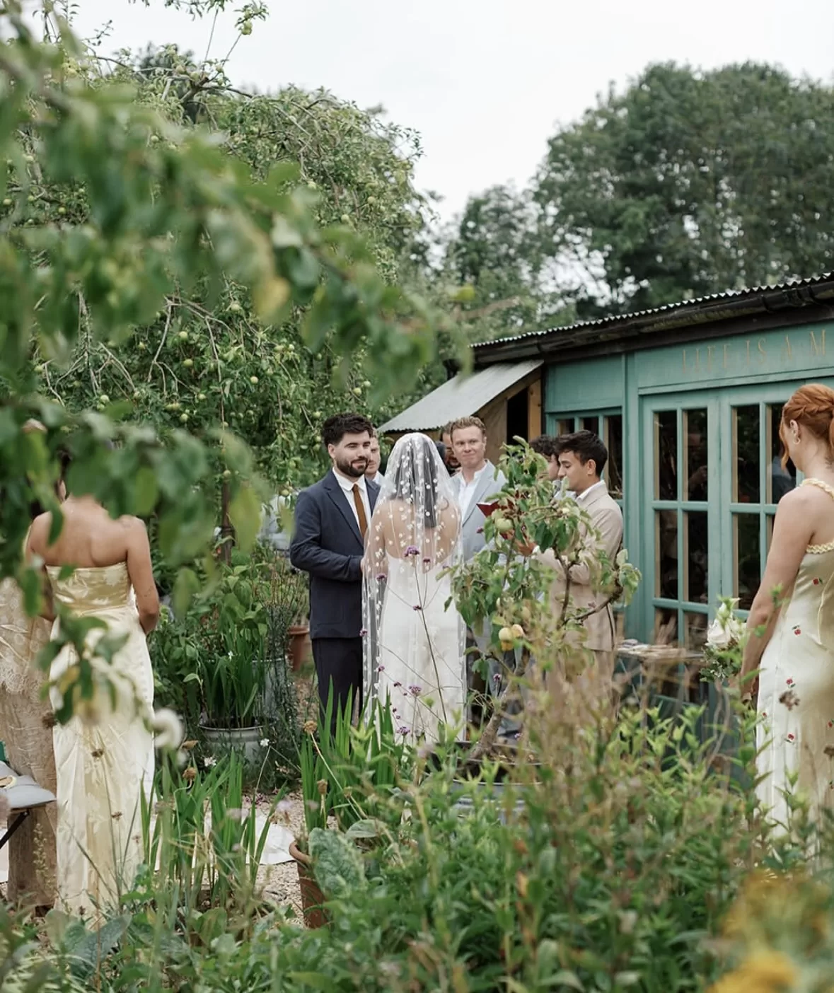 Couple exchanging vows outdoors at Worton Kitchen Garden, framed by fruit trees and soft garden foliage.