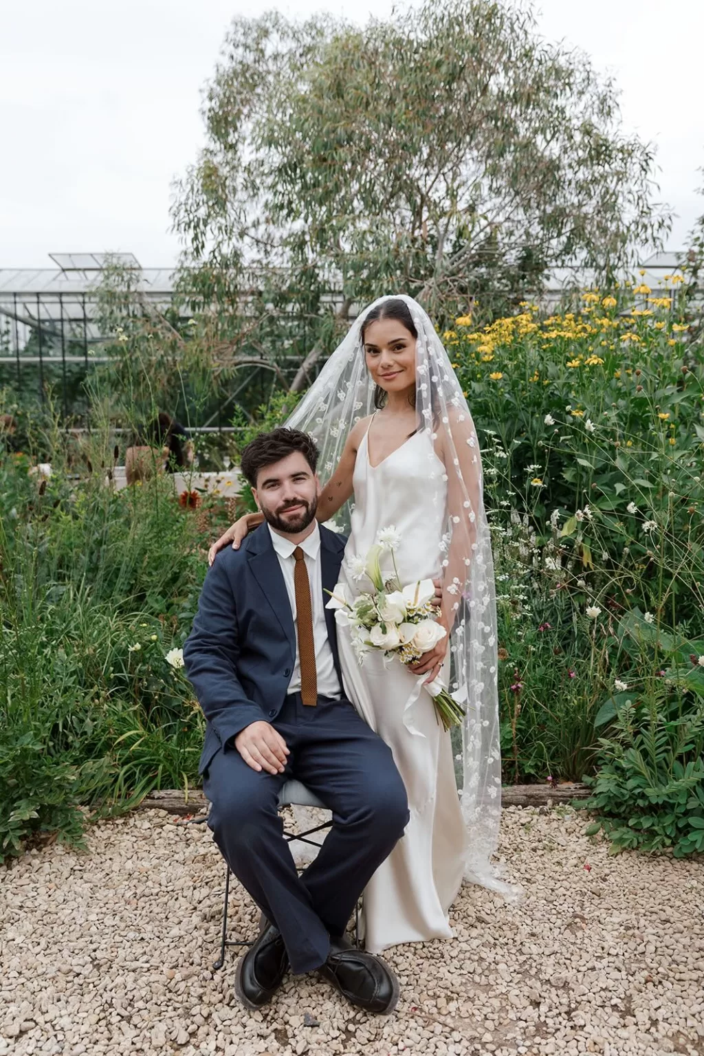 Bride and groom posing among tall garden flowers at Worton Kitchen Garden, the bride in a floral veil and holding a white bouquet.