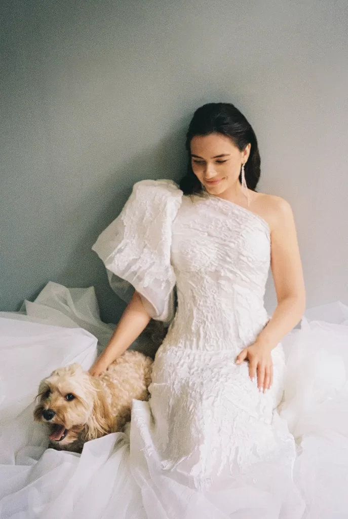 Bride seated on layers of tulle with her dog, captured in a relaxed and intimate editorial portrait.