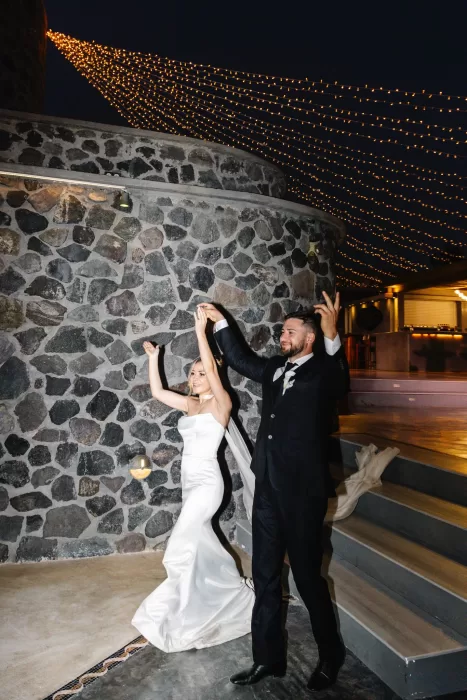 Bride and groom dancing beneath cascading string lights at Cavo Ventus, celebrating their wedding night against volcanic stone walls.