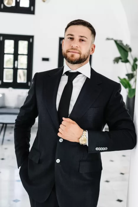 Groom dressed in a black suit during wedding preparations at Cavo Ventus, photographed inside a minimalist white interior.