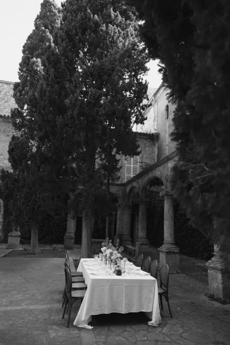 Elegant wedding dining table set beneath cypress trees in the cloister courtyard at Finca Es Convent.
