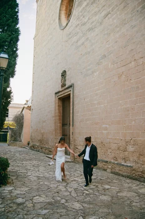 Newlyweds walking hand in hand along a historic stone street beside Finca Es Convent.