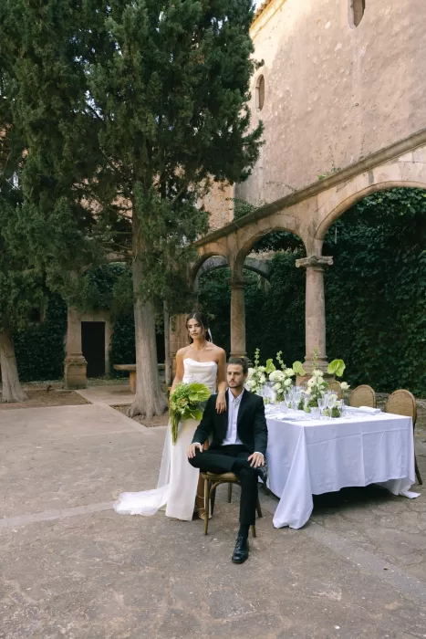 Bride and groom posed beside a dressed reception table in the courtyard of Finca Es Convent.