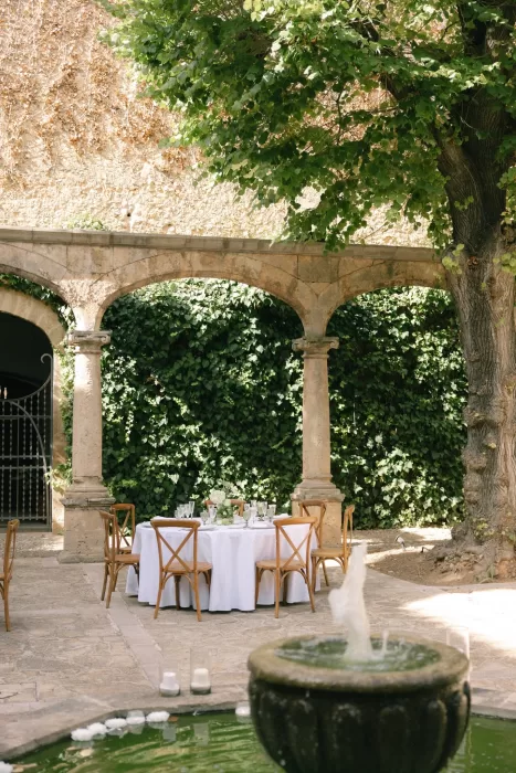 Wedding dining table set beside the fountain under stone arches in the courtyard at Finca Es Convent.