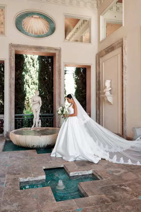 Bride standing beside an indoor fountain at Finca La Concepción, her lace-edged veil trailing elegantly behind her.