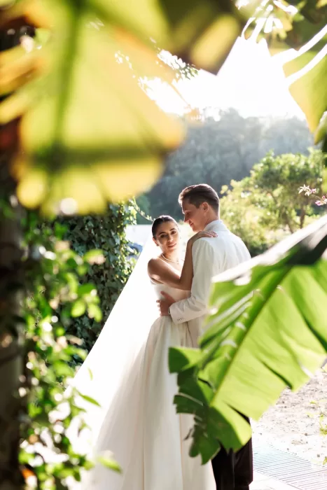 Bride and groom embracing among tropical greenery at Finca La Concepción, captured in soft natural light.