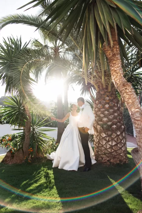Bride and groom sharing a quiet moment beneath palm trees in the gardens of Finca La Concepción at golden hour.