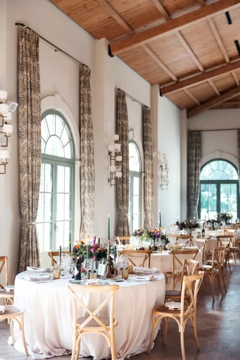 Wedding reception tables arranged inside Finca La Concepción’s light-filled hall with arched windows and wooden ceilings.