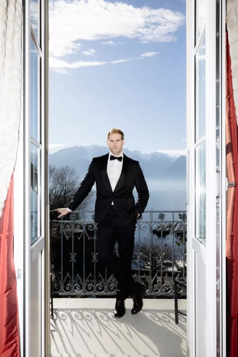 Groom standing on a balcony at Grand Hotel du Lac with lake and mountain views in the background.