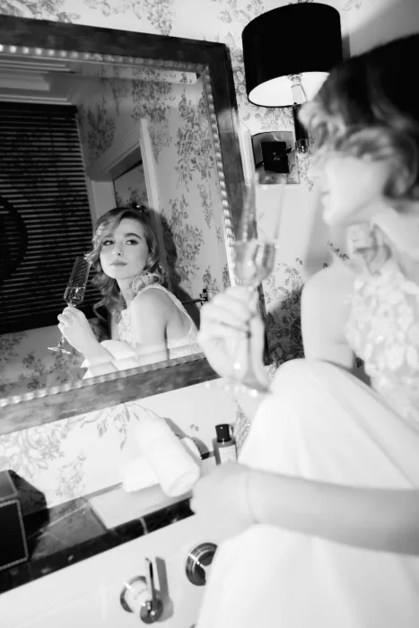 Bride reflected in a bathroom mirror holding a champagne flute inside a Grand Hotel du Lac suite, captured in a relaxed pre-reception moment.