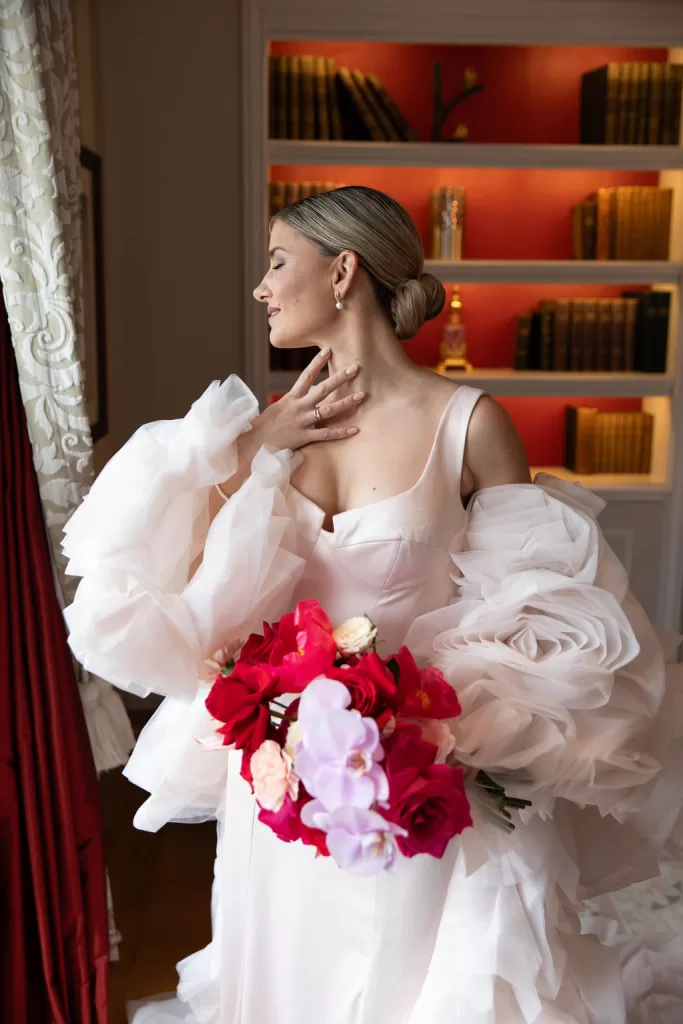 Bride holding a vibrant bouquet in an intimate library setting at Grand Hotel du Lac, captured in soft natural light.