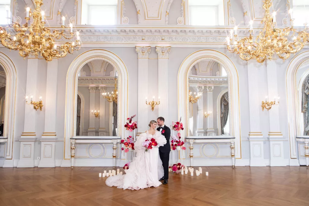 Wedding couple standing together in a grand ceremony room at Grand Hotel du Lac, framed by mirrors, chandeliers and floral arrangements.