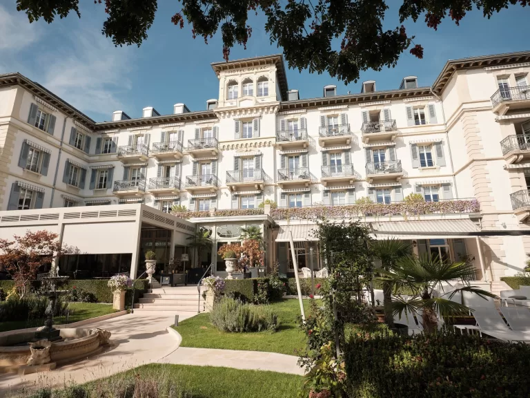 Grand Hotel du Lac façade framed by manicured gardens, capturing its refined lakeside elegance.