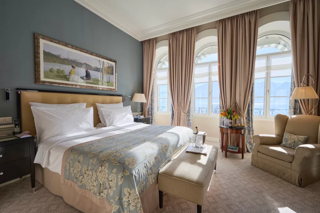 Elegant lake-view suite at Grand Hotel du Lac with soft blue tones, classic furnishings and large arched windows overlooking the water.