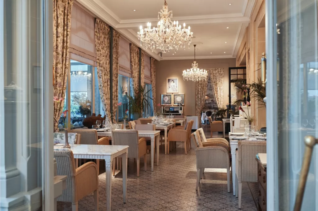 Veranda restaurant at Grand Hotel du Lac set with chandeliers, floral curtains and softly dressed tables for fine dining.
