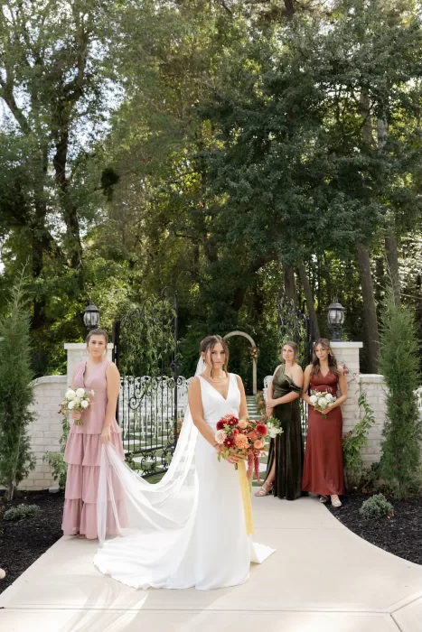 The bride stands with her bridal party at the entrance gates of The Greenhouse at Arrows Farm, framed by greenery and florals.