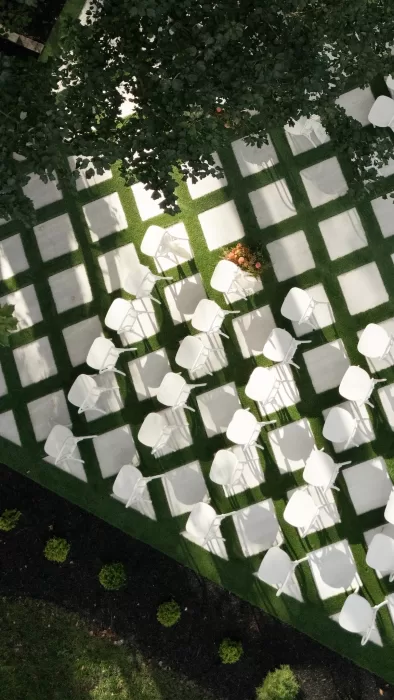 Aerial view of the outdoor ceremony layout at The Greenhouse at Arrows Farm, with white chairs arranged on a geometric lawn beneath trees.
