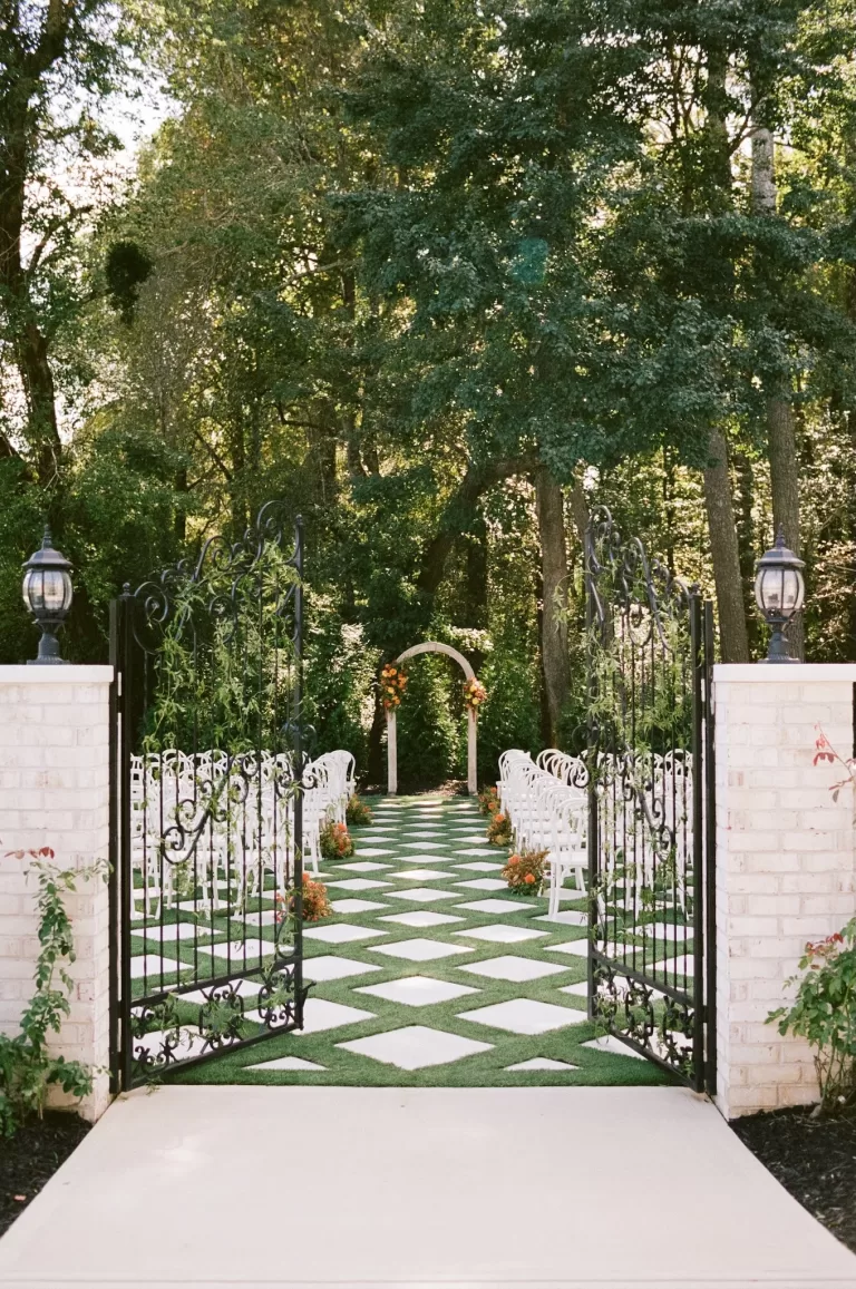The garden ceremony aisle framed by iron gates at The Greenhouse at Arrows Farm, set among lush woodland.